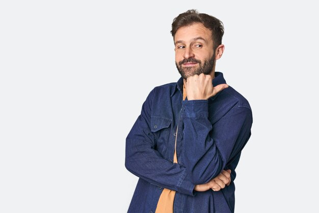 Studio portrait of young Hispanic male points with thumb finger away laughing and carefree