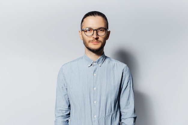 Studio portrait of young man in blue shirt wearing eyeglasses on white background