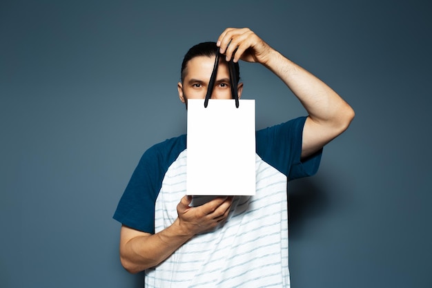 Studio portrait of young man holding a white reusable bag close to his face