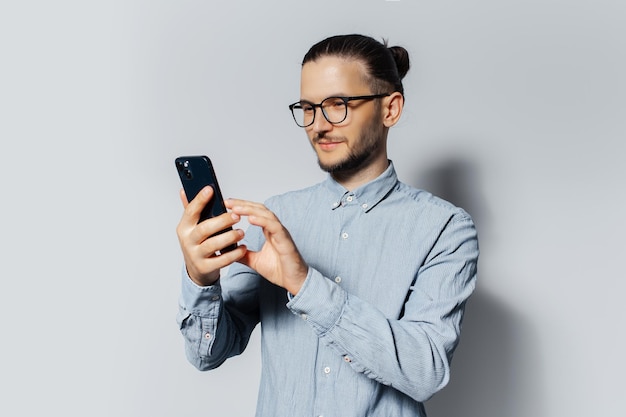 Studio portrait of young man using smartphone on white background wearing blue shirt and eyeglasses