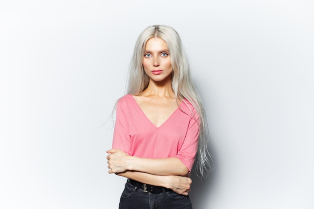 Studio portrait of young pretty smiling girl with blonde hair in pink shirt on white background