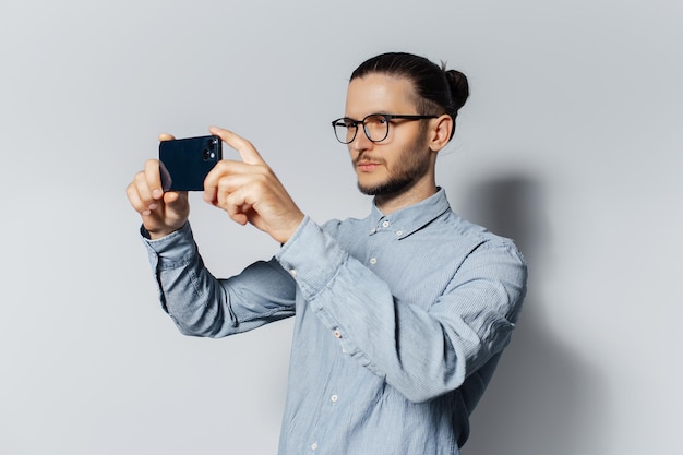 Studio portrait of young serious man making photo on smartphone on white background