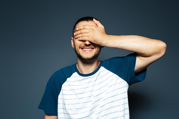 Studio portrait of young smiling man holding palm on face on blue background