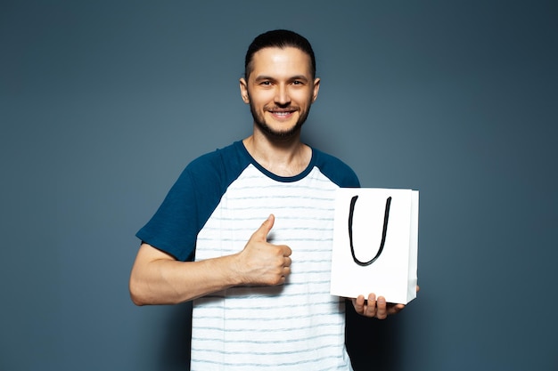 Studio portrait of young smiling man holding a white bag and showing thumb up