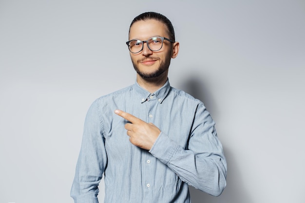 Studio portrait of young smiling man point finger away wearing eyeglasses and blue tshirt on white background