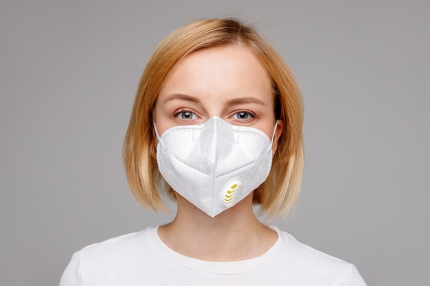 Studio portrait of young woman wearing a face mask, looking at camera, close up, isolated on gray surface. Flu epidemic, dust allergy,  protection against virus. City air pollution concept