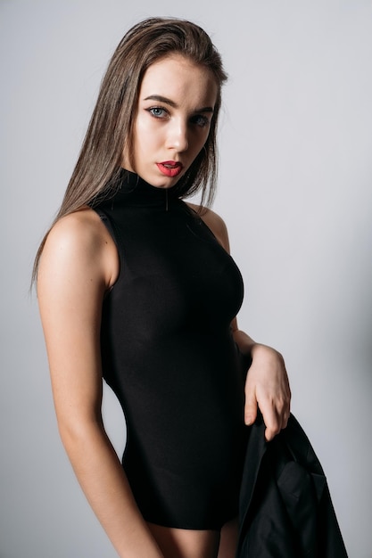 Studio portrait of young woman with long hair fashionable stylish girl in black bodysuit on grey