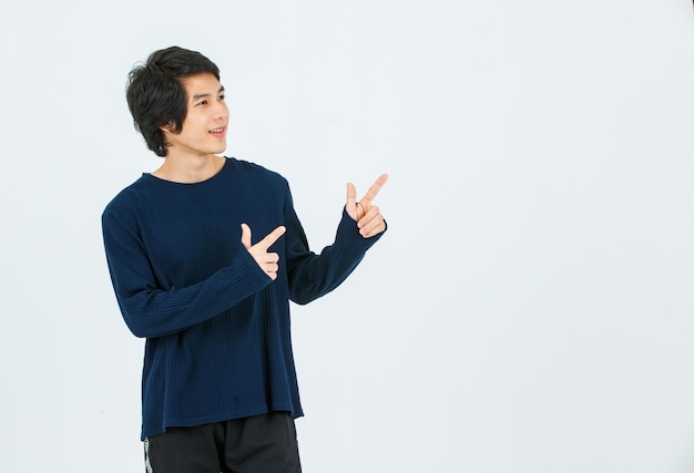 Studio shot of Asian young handsome slim teenager fashion male model in long sleeve shirt standing smiling holding hands pointing fingers on blank copy space presenting product on white background