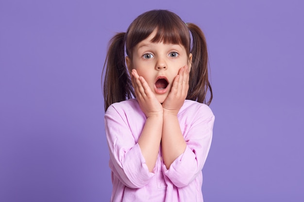 Studio shot of astonished female kid with widely opened mouth