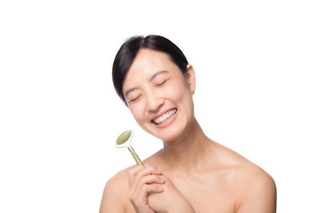 Studio shot of an attractive young asian woman using a jade roller on her face against a white background