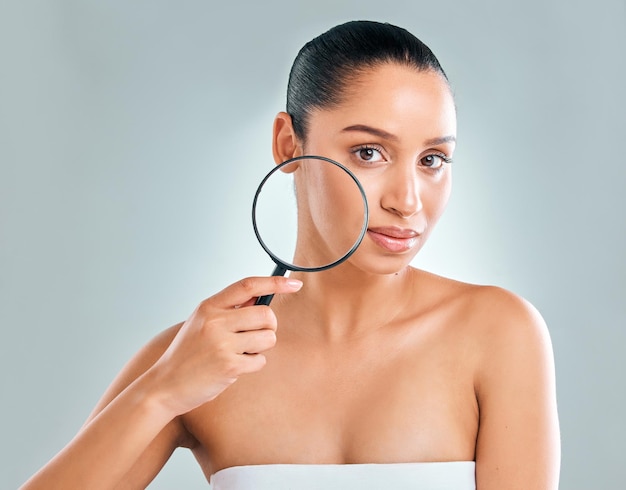 Studio shot of an attractive young woman looking through a magnifying glass against a grey background