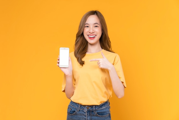 Studio shot of Beautiful Asian woman holding smartphone and smiling on light yellow background