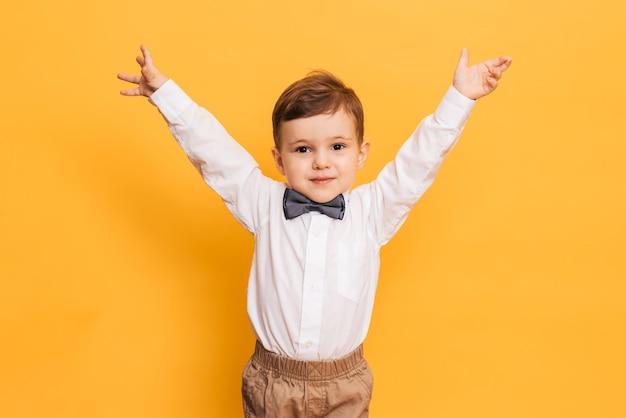 A studio shot of a cute little boy grimacing stands on a yellow background. Funny kid