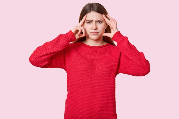 Studio shot of displeased brunette woman suffers from headache