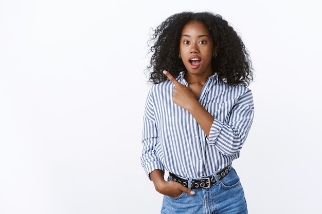 Studio shot excited thrilled emotive african american woman retelling awesome situation pointing back upper left corner open mouth amused talking stunned impressed, picking product asking question