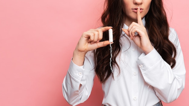 A studio shot of a girl holding a tampon in her hand in a menstrual applicator. Space for the text. The concept of feminine hygiene.