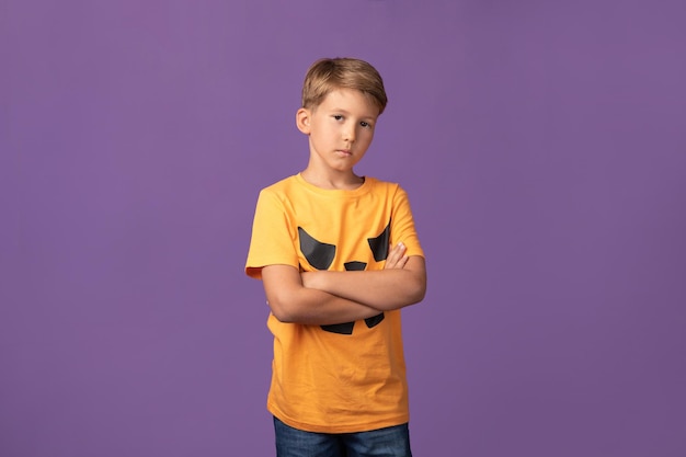 Studio shot of handsome confident preteen boy with arms crossed wearing Halloween t shirt staying against purple background