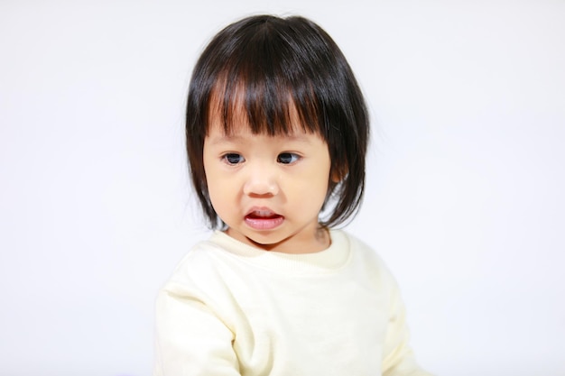 Studio shot of little cute short black hair Asian baby girl daughter model in casual plaid skirt sitting and smiling on white background