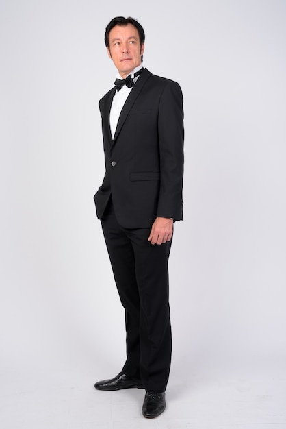 Studio shot of mature handsome businessman wearing tuxedo against white