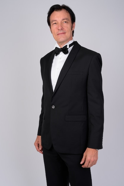 Studio shot of mature handsome businessman wearing tuxedo against white