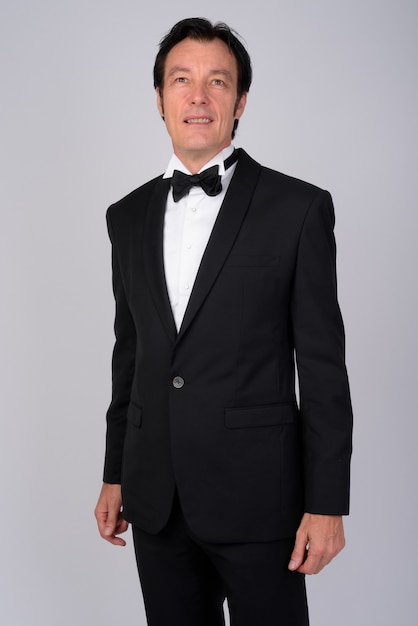 Studio shot of mature handsome businessman wearing tuxedo against white