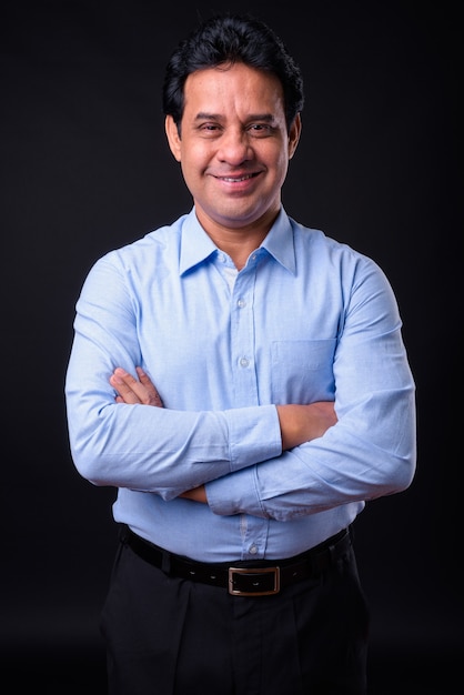 Studio shot of mature handsome Indian businessman against black background