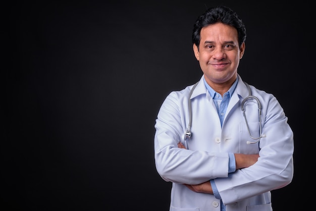 Studio shot of mature Indian man doctor against black background