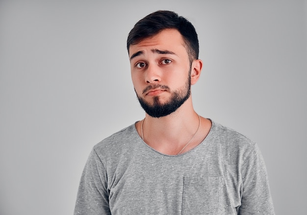 Studio shot of miserable sad attractive caucasian man with moustache and beard, being offended and upset, standing over gray background, expressing sadness and negative emotions