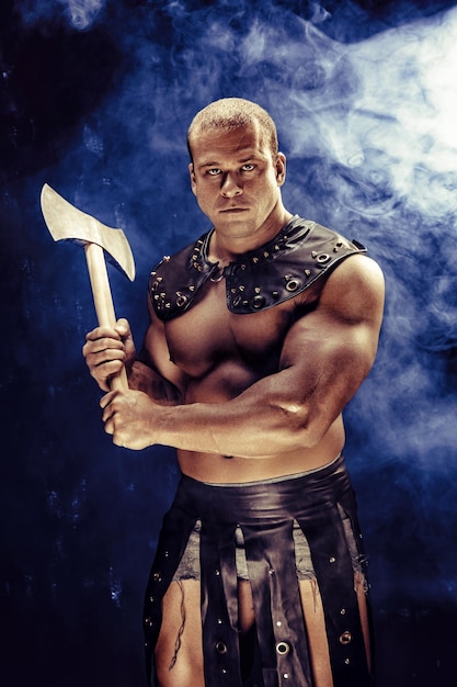 Studio shot of muscular ancient warrior man posing with axe