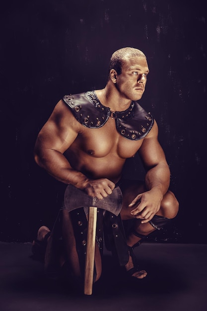 Studio shot of muscular ancient warrior man posing with axe