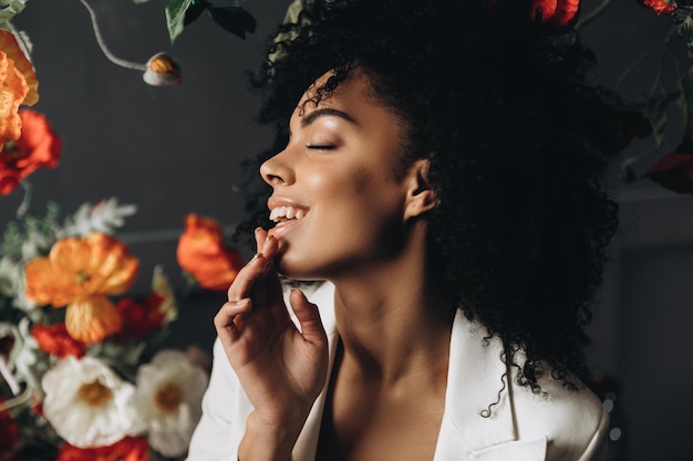 Studio shot of overjoyed dark skinned female model laughs happily and poses near flowers