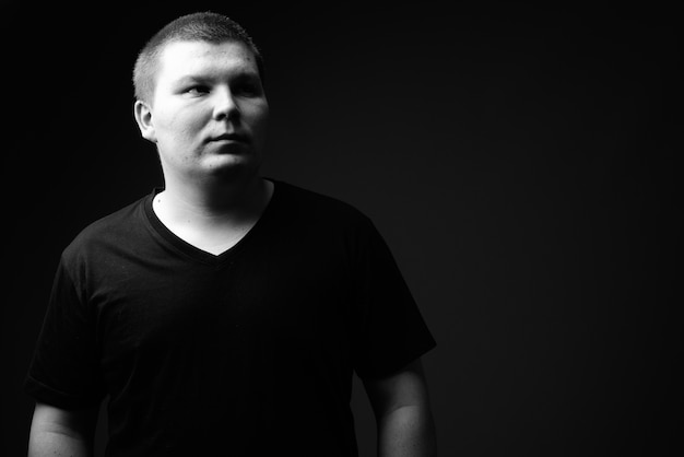 Studio shot of overweight young man against black background in black and white