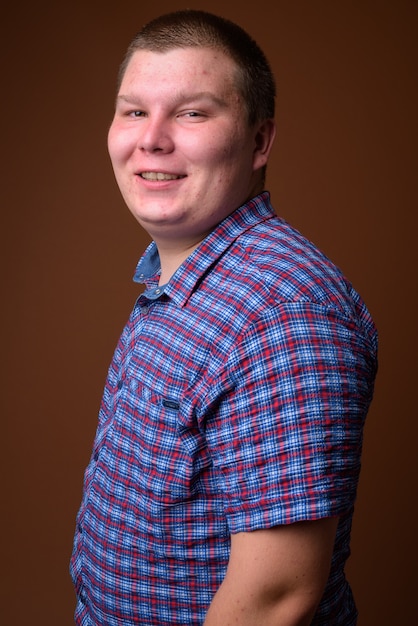 Studio shot of overweight young man wearing purple checkered shirt against brown background