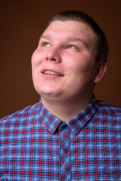 Studio shot of overweight young man wearing purple checkered shirt against brown background