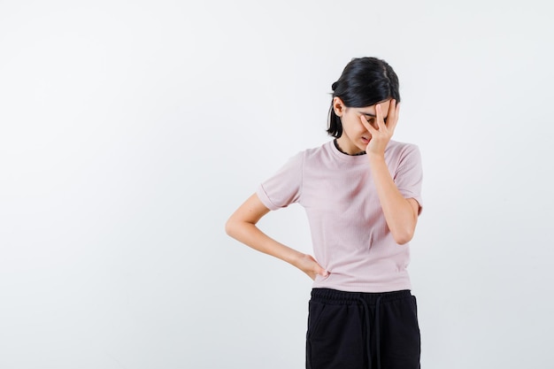 Studio shot of regretful teenager girl in ping t-shirt and choker regretfully one hand on waist other on face isolated on white background