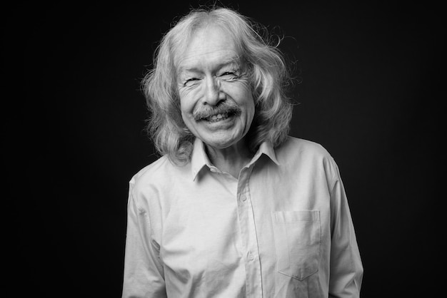 Studio shot of senior businessman with mustache wearing pink shirt against gray wall