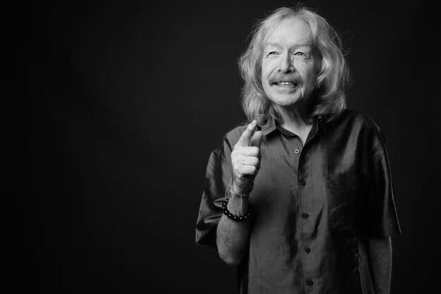 Studio shot of senior man with mustache wearing purple silky shirt against gray wall