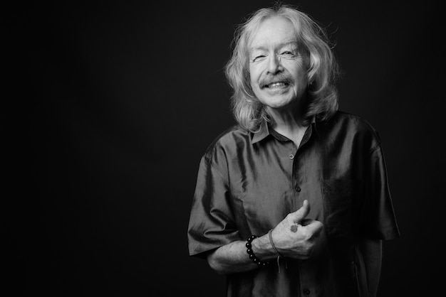 Studio shot of senior man with mustache wearing purple silky shirt against gray wall