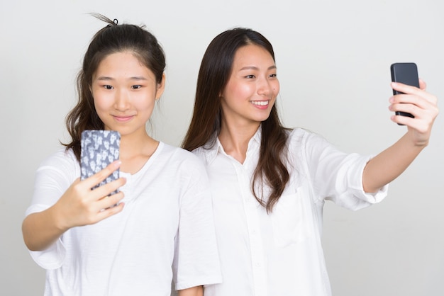 Studio shot of two young beautiful Korean women as friends together against white background