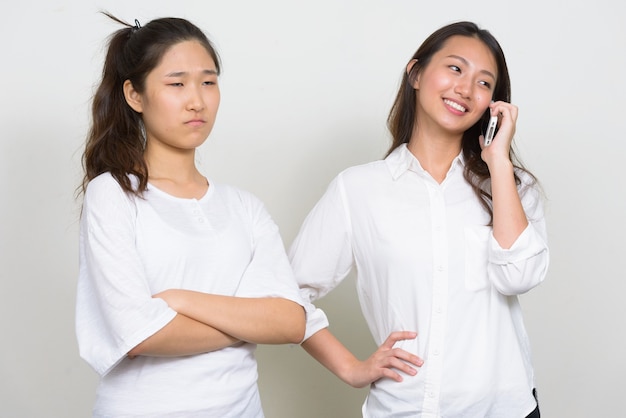 Studio shot of two young beautiful Korean women as friends together against white background