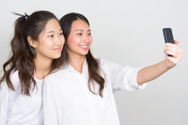 Studio shot of two young beautiful Korean women as friends together against white background