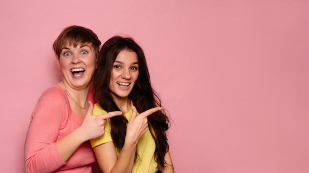 A studio shot of two young girl friends on a bright background pointing in the direction of an empty space in the background A place for your text or advertisement