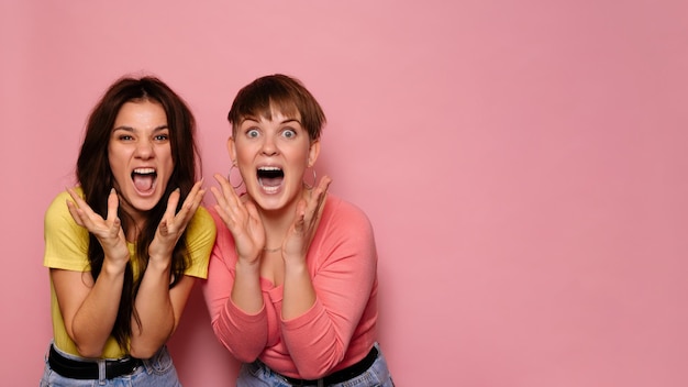 A studio shot of two young girl friends on a bright background with surprised emotions on their face A place for your text or advertisement