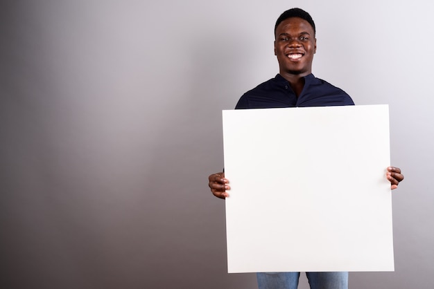 Studio shot of young African businessman holding white board against white background