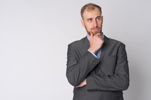 Studio shot of young bearded businessman wearing suit against white