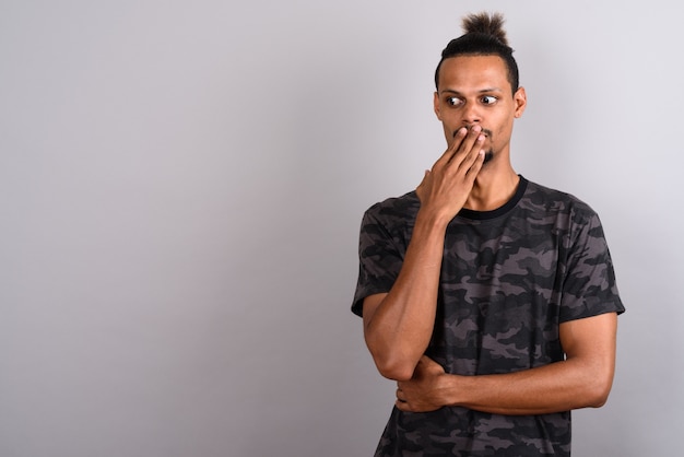 Studio shot of young bearded handsome African man wearing camouflage printed shirt with hair tied against gray background