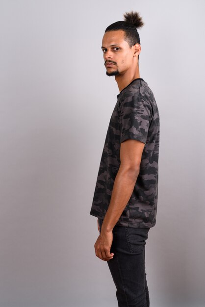 Studio shot of young bearded handsome African man wearing camouflage printed shirt with hair tied against gray background