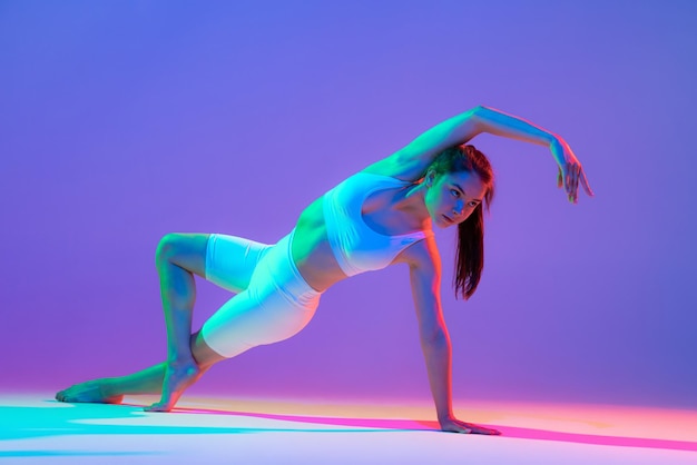 Studio shot of young flexible girl in fitness sport uniform practicing isolated on gradient