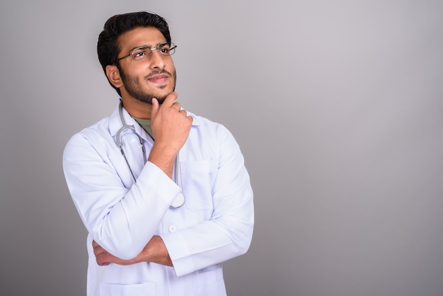 Studio shot of young handsome Indian man doctor against gray