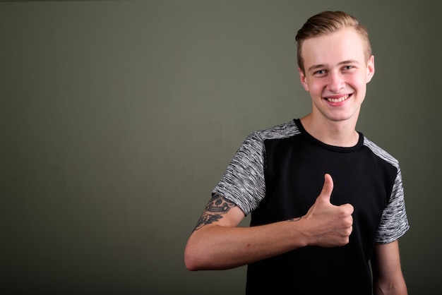 Studio shot of young handsome man with blond hair against colored background